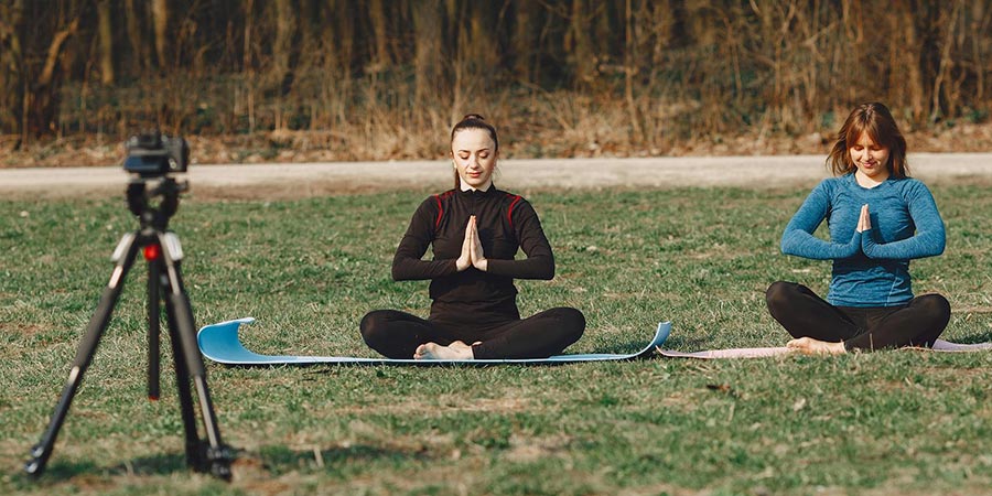 two women sitting in a Namaste pose practicing yoga outdoors